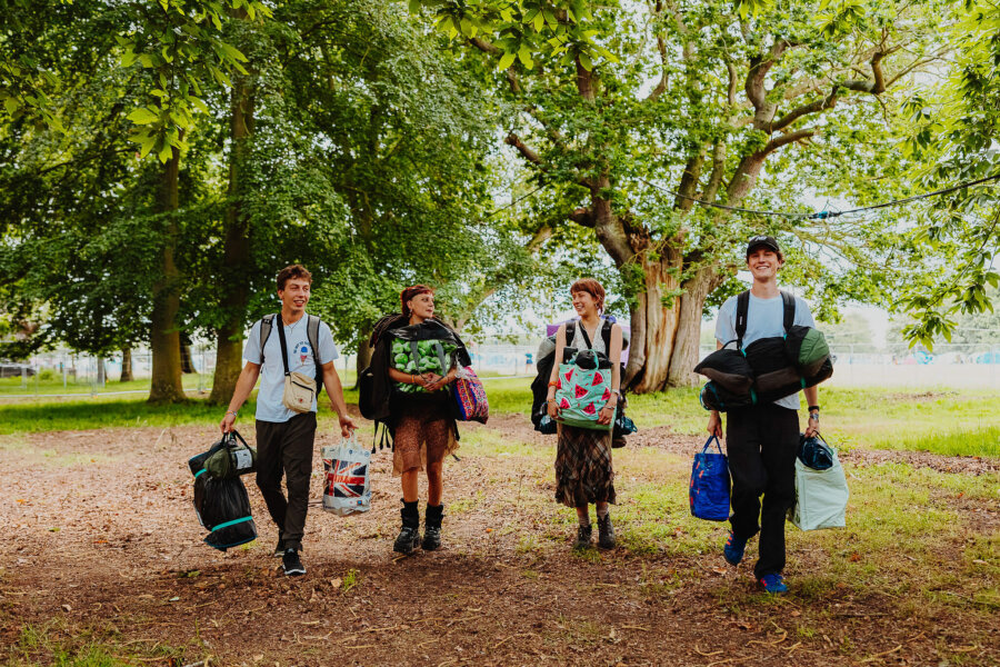 four people carrying luggage through the campsite